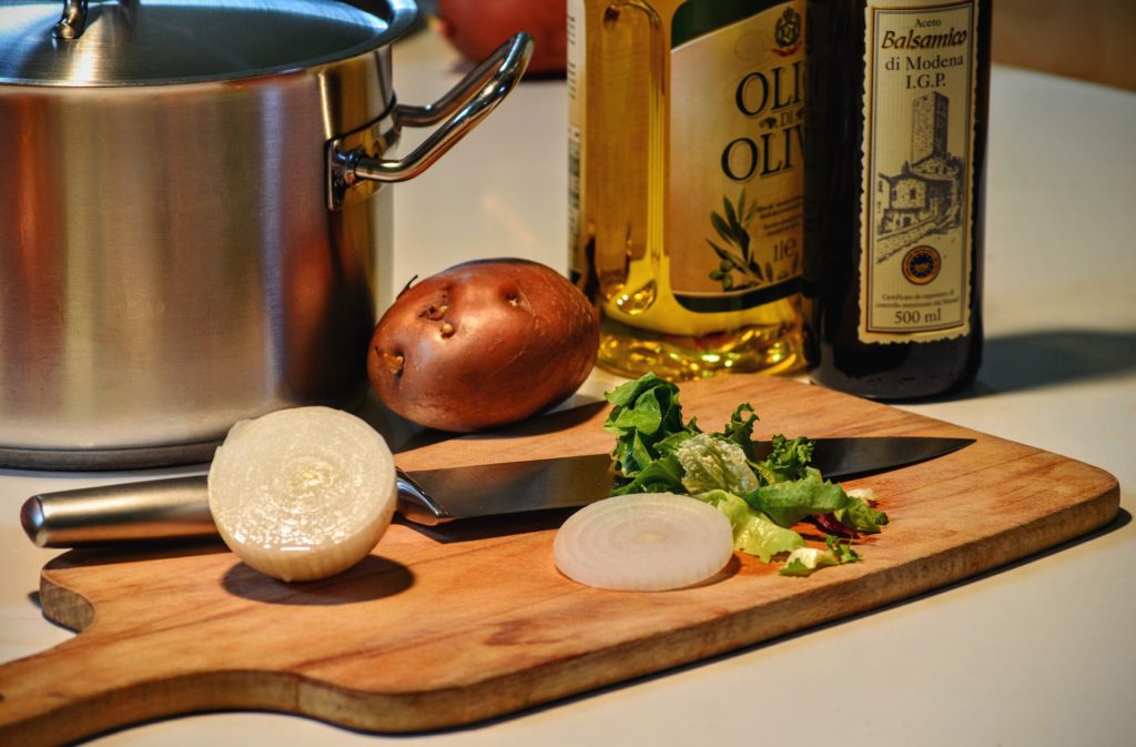 Cutting board with onion and potato. Olive oil bottles in the background. 