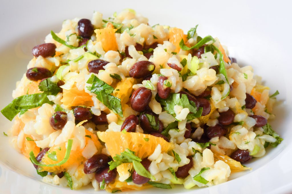 close up of brown rice, orange slices, black beans, and herbs