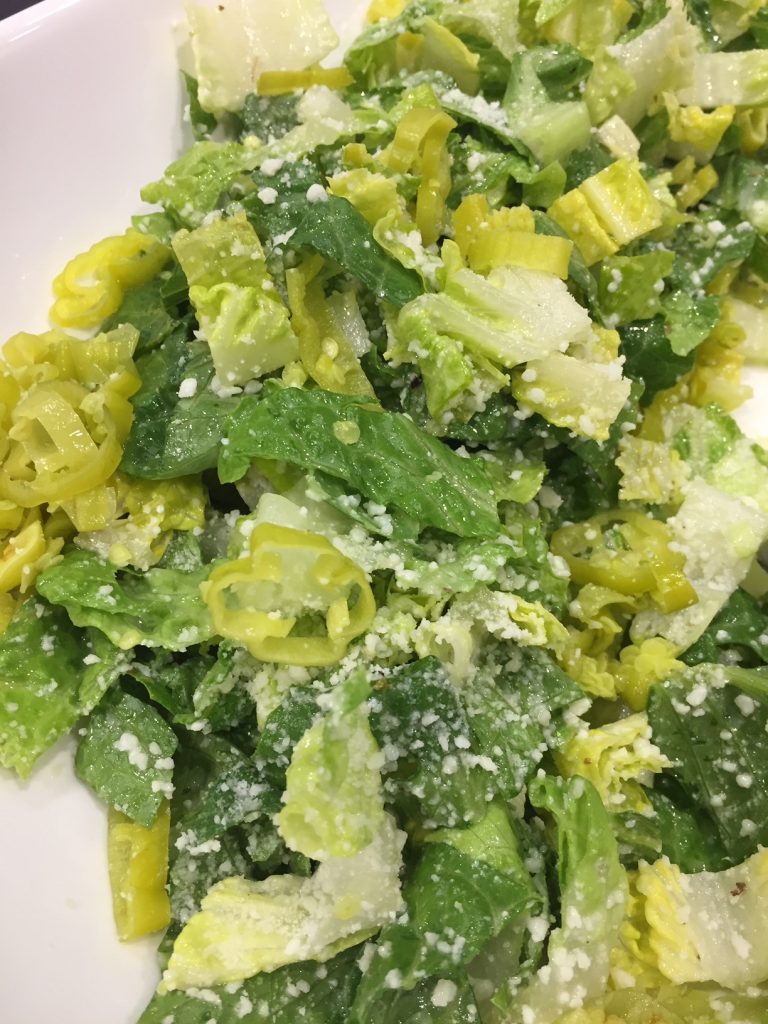 close up of romaine salad tossed with dressing and pecorino romano cheese