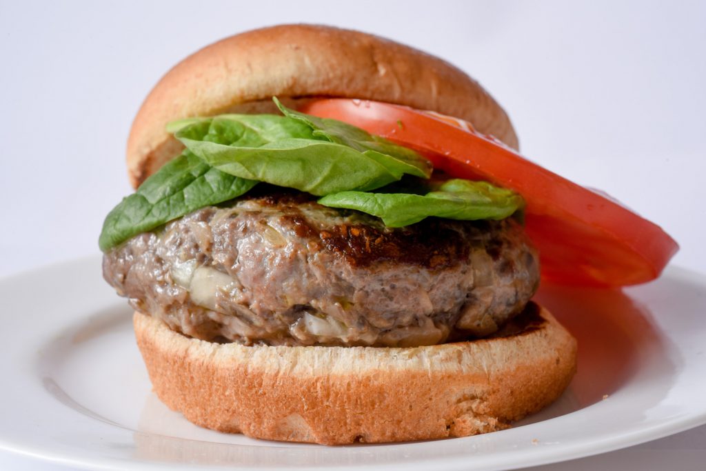 close up of a burger with a whole wheat bun, lettuce, and tomato on a white plate.