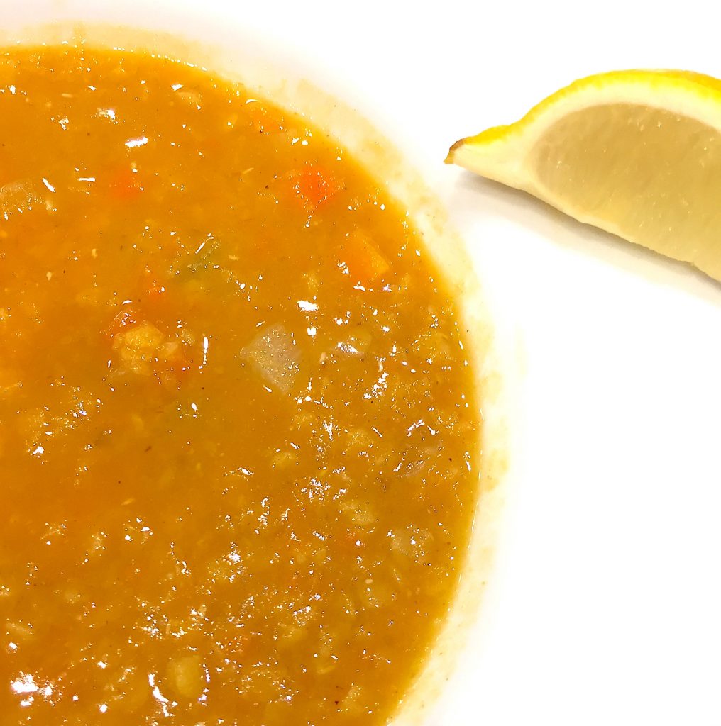 close up of bowl of red lentil soup and wedge of lemon